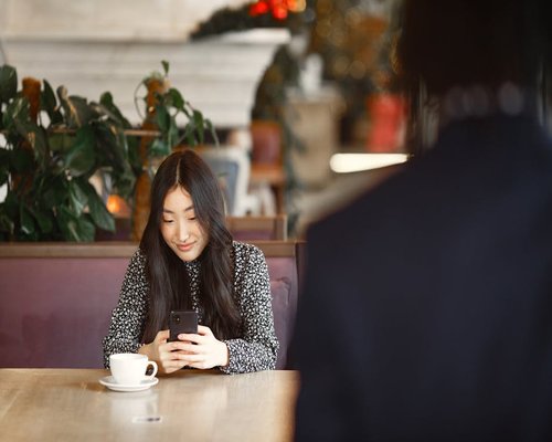 Asian woman drinking coffee and looking at her smartphone in a cafe